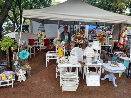 A vendor's booth at a market featuring vintage furniture, decor, and a 15-piece wicker set for sale.