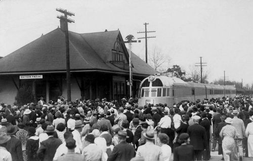 A large crowd gathers at a train station, with a vintage train arriving in Southern Pines, NC.