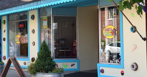 Exterior of a colorful donut shop with large windows, featuring a sign that reads "Gordy's House of Donuts."
