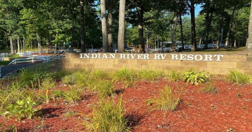 Sign for Indian River RV Resort surrounded by greenery and mulch in a wooded area.