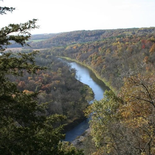A winding river flows through a valley surrounded by colorful autumn trees and rolling hills.