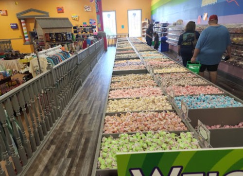 A colorful candy store aisle filled with bins of pastel marshmallows and shoppers browsing the selection.