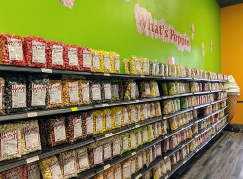 A colorful display of popcorn bags on shelves against a bright green wall with the text "What's Poppin."