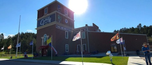 A brick building with a sign reading "Candy Co." surrounded by flags and a sunny sky in a rural setting.