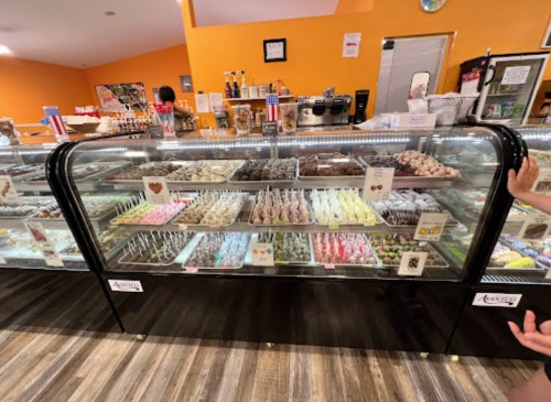 A display case filled with colorful candies and desserts, featuring various chocolates and treats in a bright shop.