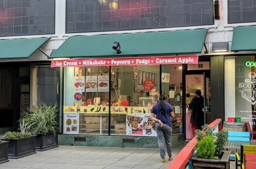 A storefront featuring a variety of treats like ice cream, milkshakes, and fudge, with green awnings and outdoor seating.