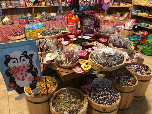 A colorful candy shop display with baskets of various candies, surrounded by festive decorations and a skunk sign.