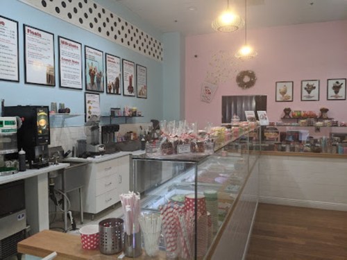 A colorful ice cream shop interior with a glass display case, menu boards, and various treats on the counter.