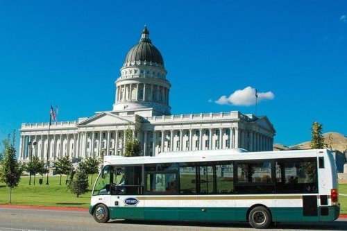 A bus parked in front of a grand government building with a dome, under a clear blue sky.