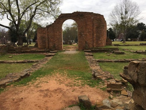 Ruins of a brick archway surrounded by grassy grounds and scattered stone remnants of an old structure.