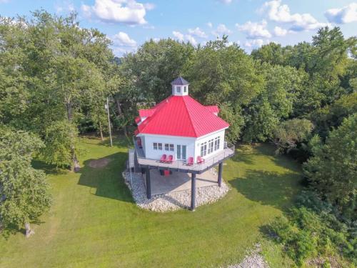 Aerial view of a unique red-roofed house on stilts, surrounded by lush greenery and blue skies.