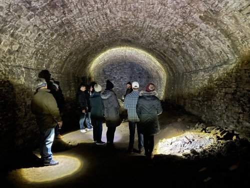 A group of people exploring a dimly lit stone tunnel with arched ceilings and a rocky floor.
