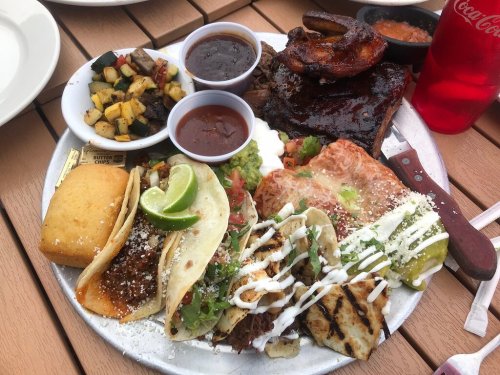 A colorful platter featuring tacos, grilled chicken, beef, rice, beans, and sides of salsa and vegetables.