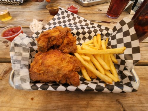A basket with two pieces of fried chicken and a side of French fries, served on a checkered paper.