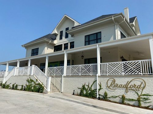 A large, modern white house with a porch and decorative railings, featuring the name "Bradford" on the wall.