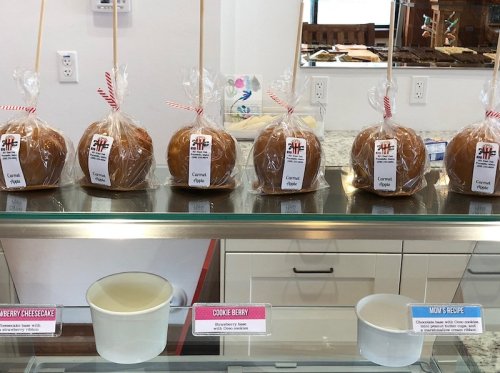 A display of caramel apples in clear bags, labeled with flavors, on a counter in a shop.