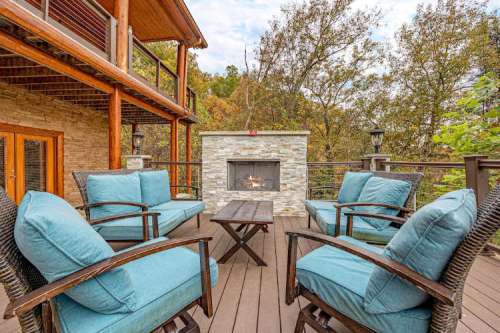 Cozy outdoor seating area with blue cushions, a stone fireplace, and autumn foliage in the background.