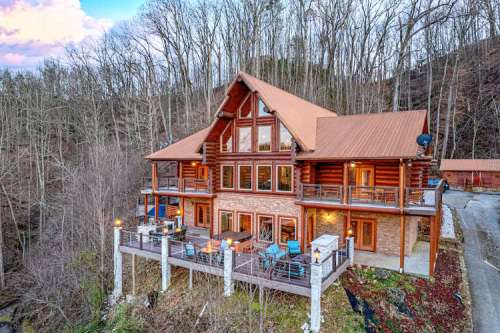 A large log cabin with multiple balconies, surrounded by trees and a scenic hillside.