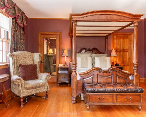 A cozy bedroom featuring a four-poster bed, elegant armchair, and warm wooden accents.