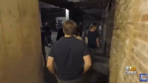 A group of people walking through a dimly lit, brick-walled corridor in a basement.