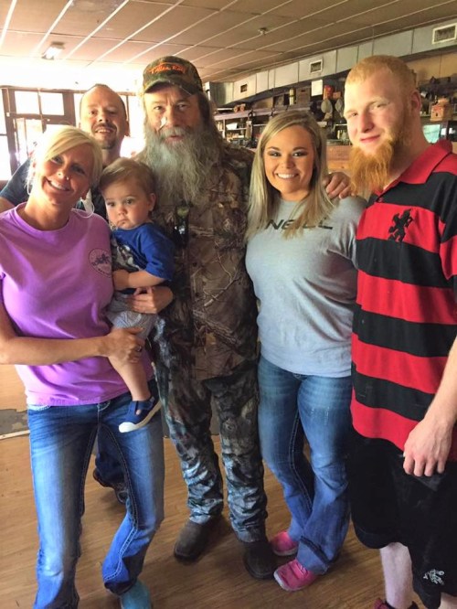 A group of five people, including a man in camouflage, posing together in a rustic indoor setting.