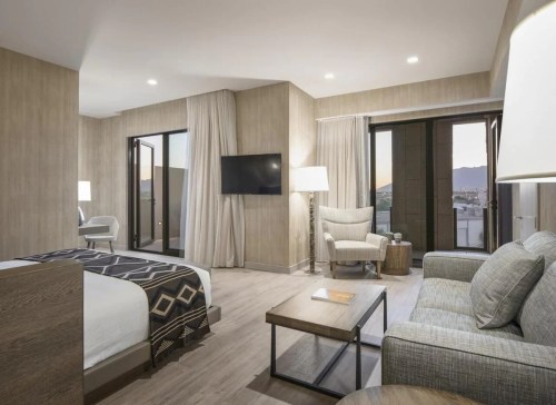 Modern hotel room featuring a bed, seating area, large windows, and stylish decor.