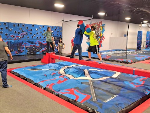 A group of people enjoying an indoor activity center with climbing walls and inflatable obstacles.