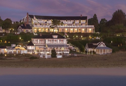 A coastal hotel at dusk, featuring multiple buildings with lights and lush greenery surrounding the property.