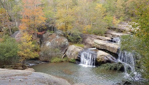 A serene landscape featuring a waterfall cascading over rocks, surrounded by colorful autumn foliage and a calm river.