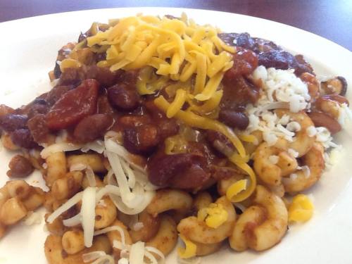 A plate of pasta topped with chili, beans, and a mix of shredded cheeses.