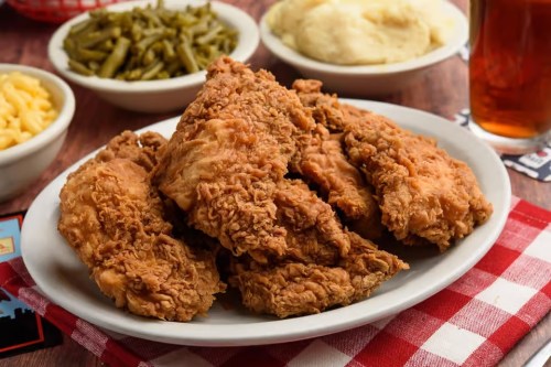 A plate of crispy fried chicken with sides of green beans, mashed potatoes, and macaroni and cheese.