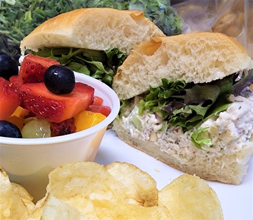 A sandwich filled with chicken salad and lettuce, served with a side of mixed fruit and potato chips.