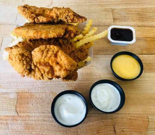 A serving of crispy fried chicken tenders with crinkle-cut fries and three dipping sauces on a wooden surface.