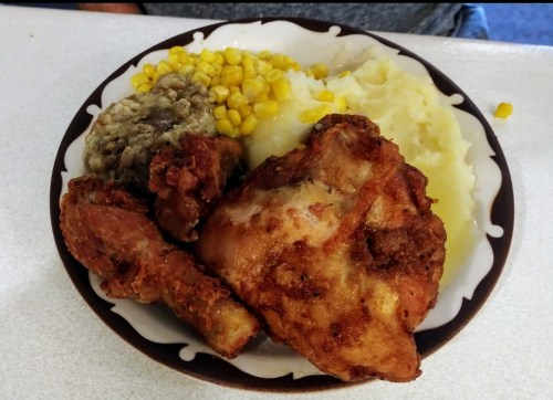 A plate of fried chicken, mashed potatoes, corn, and stuffing, served on a decorative dish.