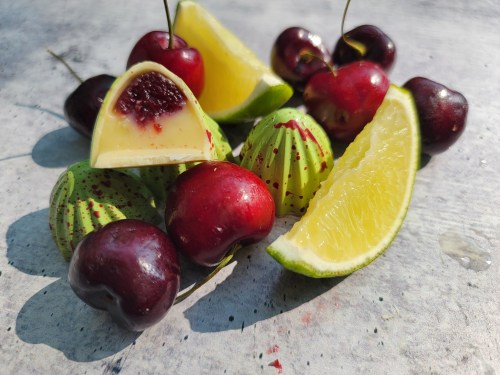 A colorful arrangement of cherries, lime wedges, and green candies on a textured surface.