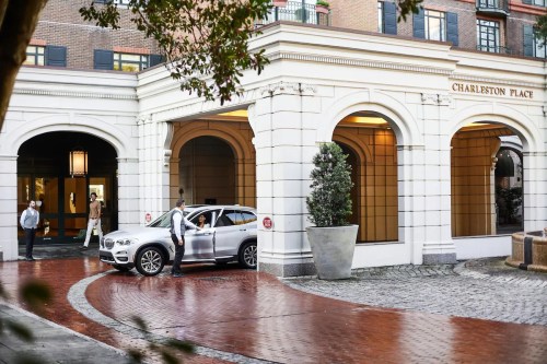 A silver SUV parked at the entrance of Charleston Place, with two people standing nearby in a stylish urban setting.