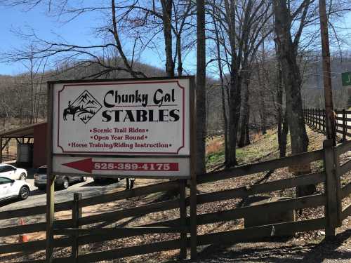 Sign for Chunky Gal Stables, featuring scenic trail rides and horse training, surrounded by trees and a wooden fence.