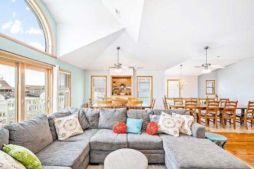 Bright, airy living space with a gray sectional sofa, colorful pillows, and a dining area featuring wooden chairs and a table.