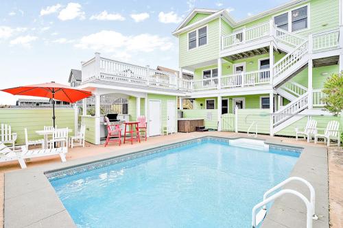 A bright green house with a pool, patio furniture, and an umbrella, surrounded by a sunny outdoor area.