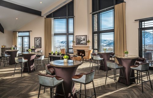 A stylish event space with tall windows, modern furniture, and a fireplace, offering mountain views.