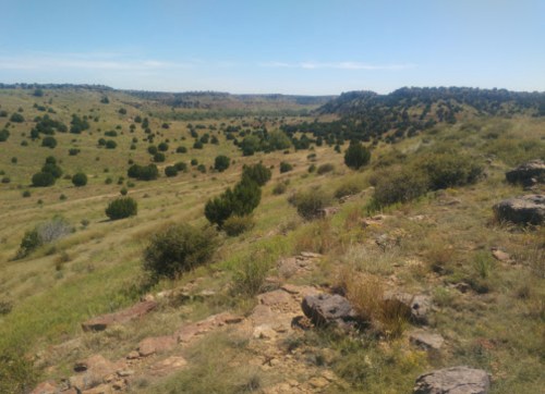A scenic view of rolling hills and green vegetation under a clear blue sky.