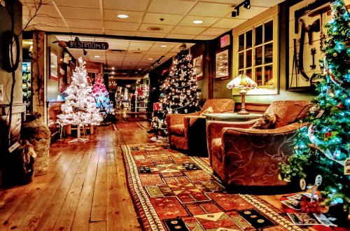 Cozy hallway decorated for Christmas with multiple trees, festive lights, and comfortable seating.