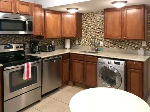 Modern kitchen with wooden cabinets, stainless steel appliances, and a washing machine, featuring a tiled backsplash.