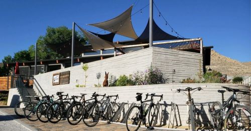 Bicycles lined up in front of a modern building with shade sails and landscaping under a clear blue sky.