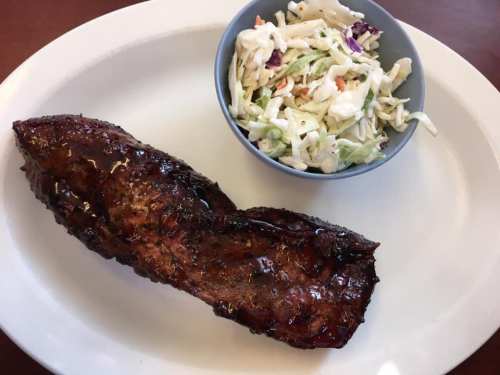 A plate with a grilled meat portion and a small bowl of coleslaw on the side.