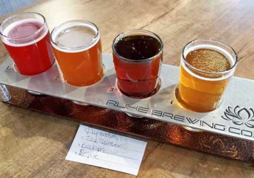 A flight of four craft beers in small glasses on a wooden table, with a note listing their names.