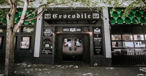 Entrance of the Crocodile bar, featuring a dark facade and green decorative awnings, surrounded by trees.