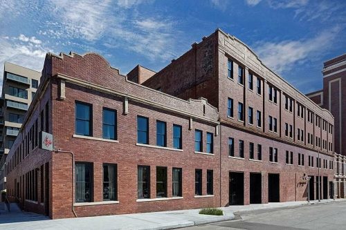 Historic brick building with large windows, featuring a mix of architectural styles under a blue sky.