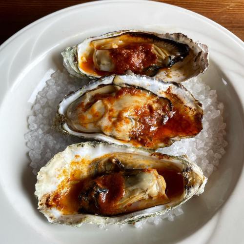 Three oysters on a bed of ice, topped with a spicy red sauce, served on a white plate.