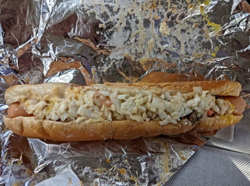 A hot dog in a bun topped with coleslaw, wrapped in crinkled aluminum foil.